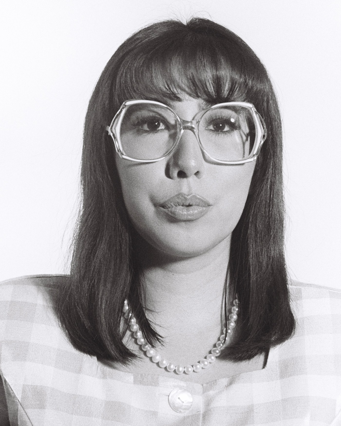 Black and white portrait of Leslie Hurtado wearing oversized glasses and a pearl necklace